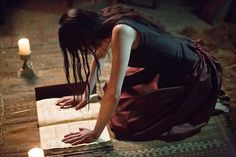 a woman kneeling down reading a book next to a candle