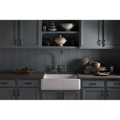 a kitchen with gray cabinets and a white farmhouse sink in the center is surrounded by dishes