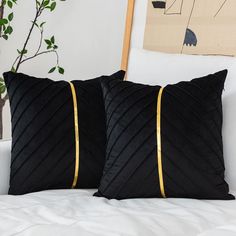 two black and gold pillows sitting on top of a white bed next to a plant