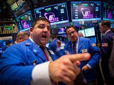 two men in blue jackets talking to each other on the floor of a stock market