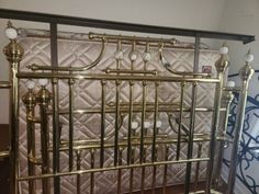 a gold metal baby crib with white balls on the top and bottom rails, in front of a wall