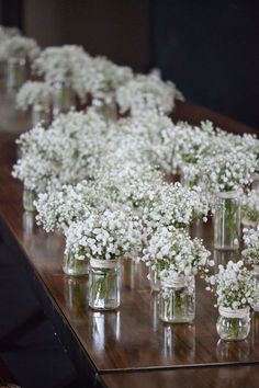 small glass vases filled with baby's breath flowers on a wooden table top