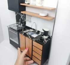 a hand is pointing at a miniature kitchen with black and white marble counter tops,