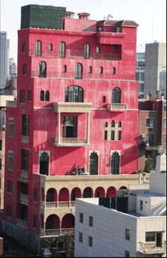 an old red building with many windows and balconies on the top floor, in front of other buildings