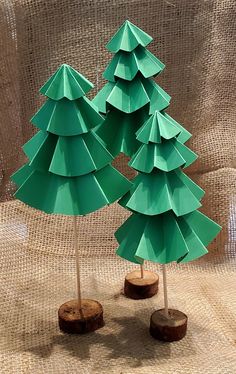 three green paper christmas trees sitting on top of a wooden table next to each other