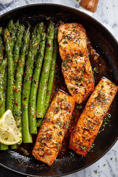 salmon and asparagus in a skillet with lemon wedges