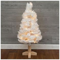 a white artificial christmas tree with lights on the base and wooden stand in front of a wall