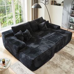 a large black couch sitting on top of a wooden floor next to a lamp and window