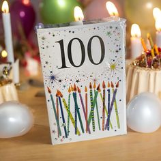 a birthday card with candles on it sitting in front of some cupcakes and balloons