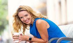 a woman sitting on a bench holding a coffee cup and looking at the camera while smiling