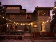 a house is decorated with christmas lights and string lights as a woman climbs the ladder