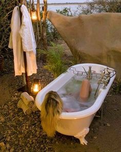 a woman taking a bath in a white tub next to some rocks and trees with candles