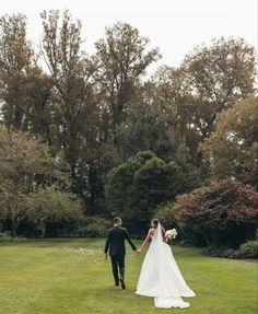 a bride and groom holding hands walking through the grass