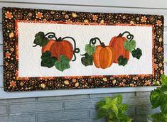 a wall hanging with three pumpkins and green leaves on the side of a house