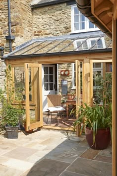 a small wooden building with glass doors and windows on the side of it, surrounded by potted plants