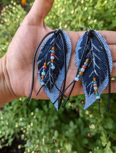 two pairs of blue feather earrings with beaded details on the ends, held in a person's hand