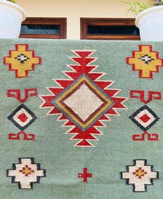 a green rug with red, yellow and blue designs on it next to a potted plant