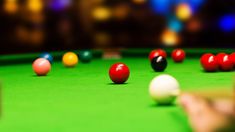 a pool table with several different colored balls on it and one person's hand reaching for the ball