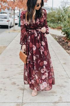 a woman in a long dress and hat is walking down the sidewalk with her hand on her hip