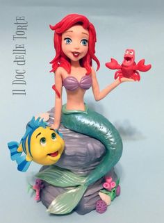 the little mermaid figurine is sitting on top of a rock with a fish