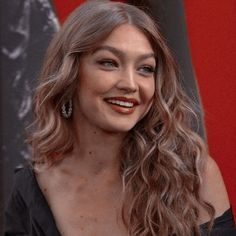 a woman with long hair smiling at the camera while standing in front of a red wall