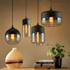 three lights hanging from the ceiling above a table with books and vases on it