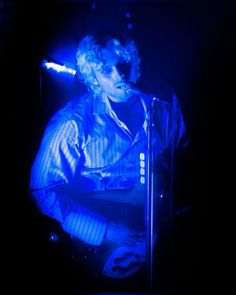 a man with blonde hair playing a guitar in front of a microphone and some blue lights