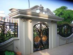 a white gate with two golden bells on it's top and bottom, in front of a house