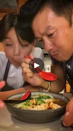 a man and woman looking at a bowl of food with chopsticks in it