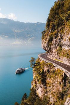 a boat traveling on the water near a cliff with a road going up it's side