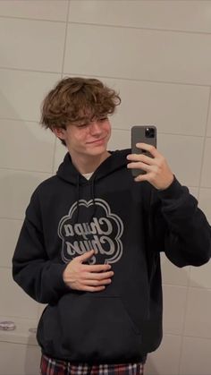 a young man taking a selfie in front of a mirror wearing a black chupa chups hoodie