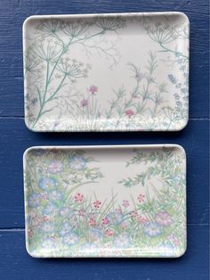 two plates with flowers painted on them sitting next to each other in front of a blue wall