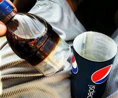 a person is holding a pepsi bottle and a cup in their lap while sitting down