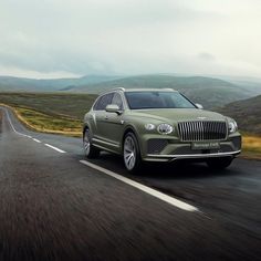 a green car driving down the road with mountains in the background