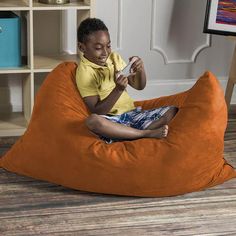 a young boy sitting on an orange bean bag chair holding a game controller in his hand