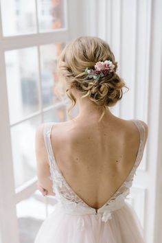 the back of a bride's dress with flowers in her hair, looking out a window