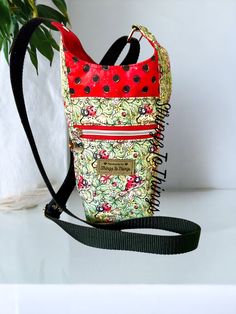 a small purse with a red and black polka dot design on the front, sitting next to a green plant