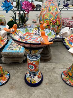 colorfully painted vases and birds on display at an outdoor market place with flowers in the background