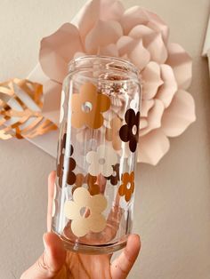 a person holding up a clear glass with flowers on the side and gold foiling