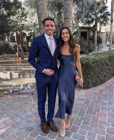 a man and woman standing next to each other on a brick walkway in front of palm trees