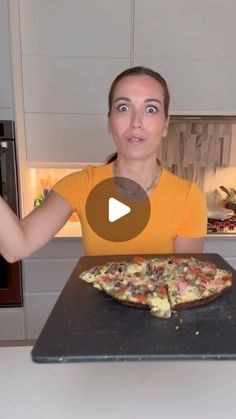 a woman standing in front of a pizza on a pan with one hand up and the other