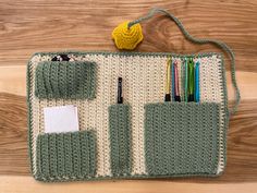 a crocheted purse with some pens and pencils in it on top of a wooden floor