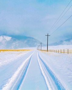 a road that is covered in snow with power lines above it and mountains in the distance