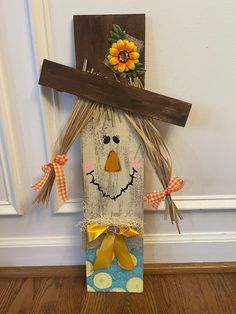 a scarecrow made out of scrap wood on the floor with sunflowers hanging from it's head