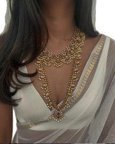 a woman wearing a white top and gold jewelry on her chest, with long dark hair