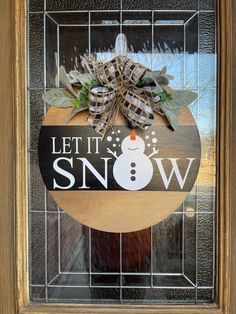 a wooden sign that says let it snow with a snowman on the front door