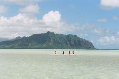 three people riding surfboards on top of a large body of water with mountains in the background