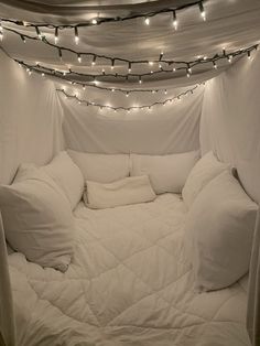 a bed covered in white sheets and pillows with lights on the ceiling above it at night