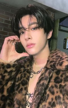 a young man in a leopard print coat posing for the camera with his hand on his ear