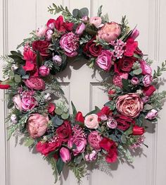 a wreath with pink and red flowers hanging on a door